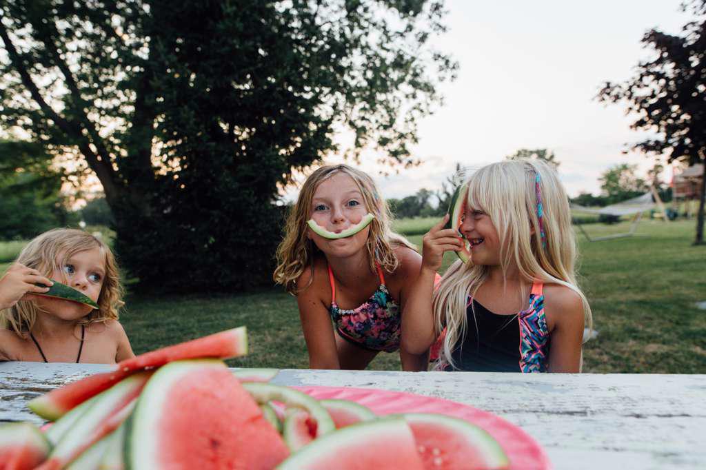 YOUNG KIDS BEING SILLY WHILE EATING WATERMELON OUTSIDE IN THE SUMMER