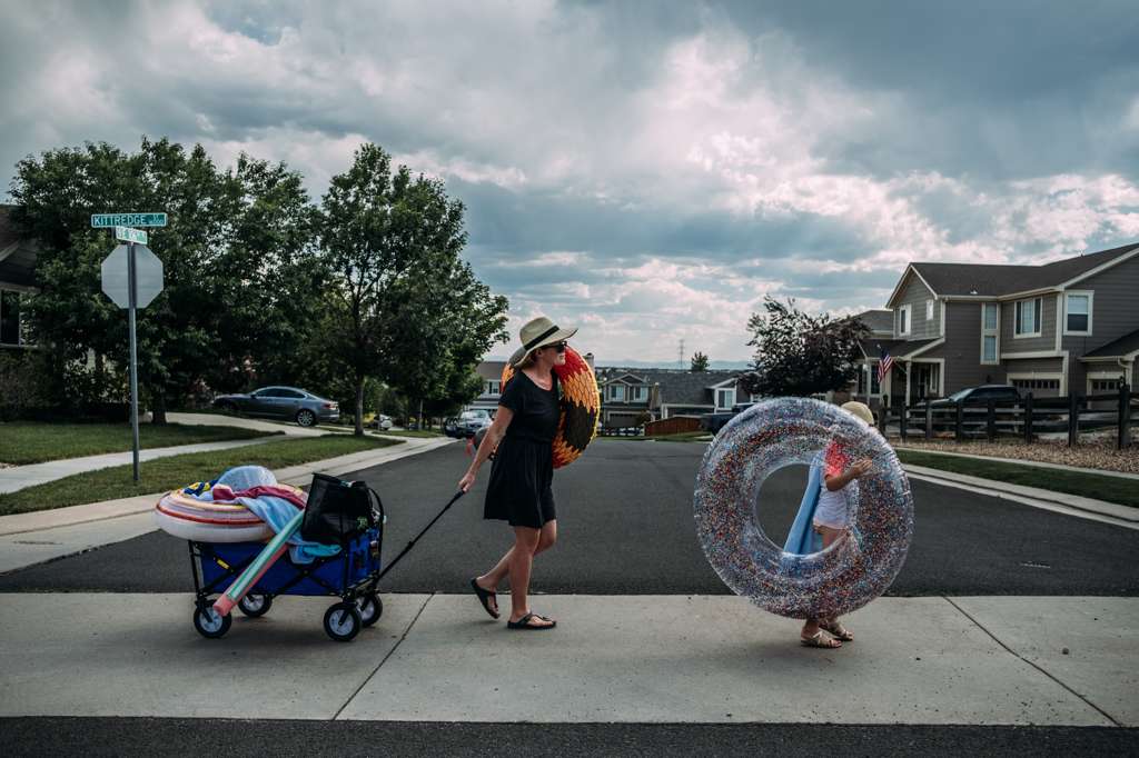 MOM WALKING WITH DAUGHTER CARRYING POOL TOYS ON SUMMER DAY