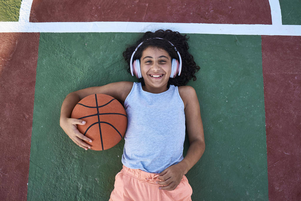 A little girl with curly hair is lying on a basketball court laughing